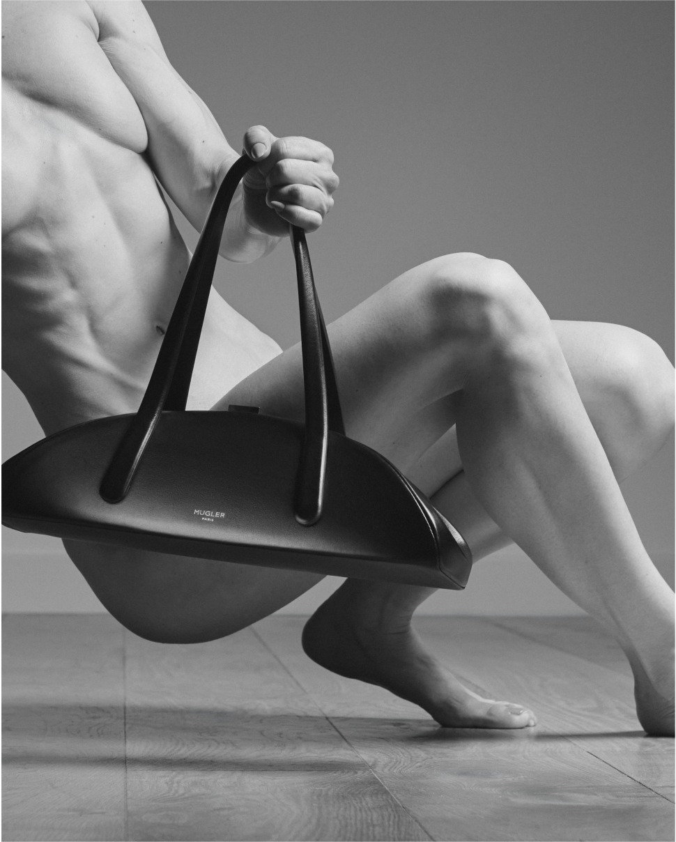 Fisiculturista sentada no chão segura pelas alças a bolsa Lua preta da Mugler